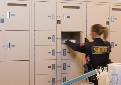 Gray evidence lockers of different sizes set against a blue brick wall in a spacious room.