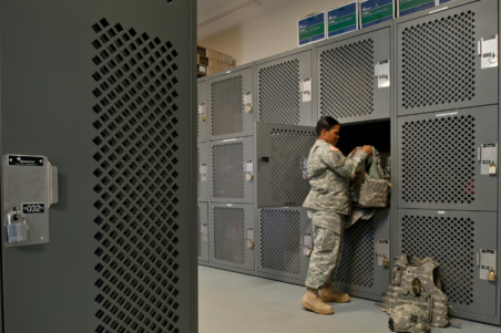 Female soldier in uniform at military base, storing personal gear in locker room.