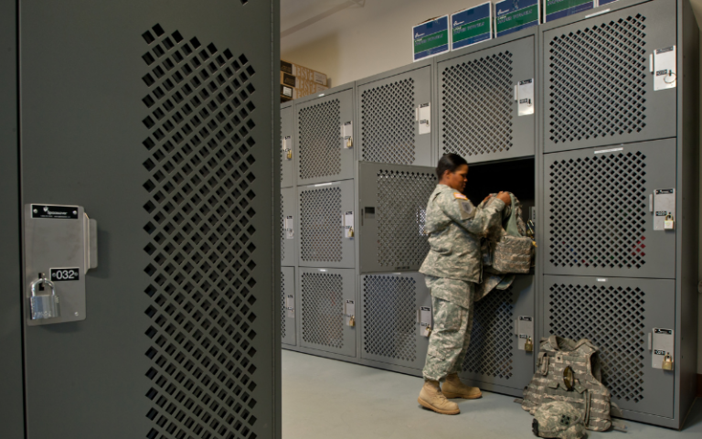 Female soldier in uniform at military base, storing personal gear in locker room.