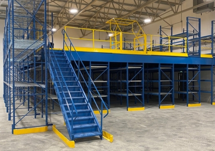 : A wide view of a warehouse filled with blue and yellow shelves, highlighting a mezzanine pallet rack system for storage.