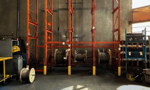 Warehouse racking system holding wire rolls on orange beams.