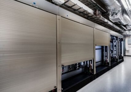 A well-lit hallway featuring silver security shutters in a warehouse environment.