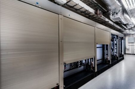 A well-lit hallway featuring silver security shutters in a warehouse environment.