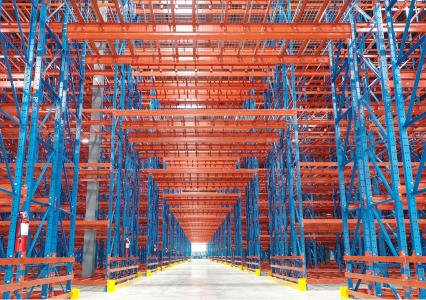 A vast warehouse showcasing an orange and blue structural racking system with yellow protectors.