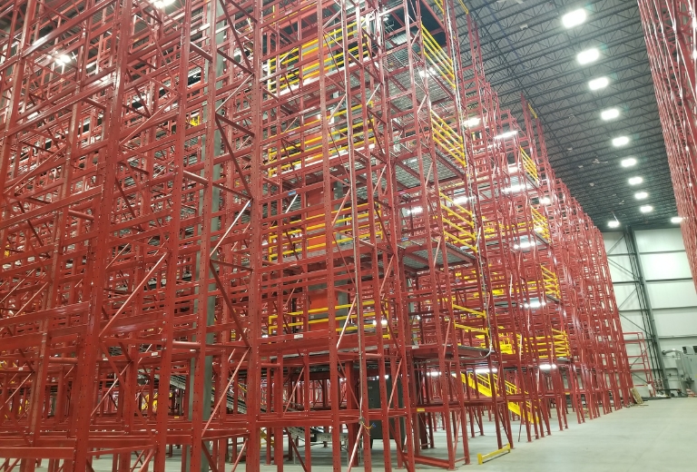 : A warehouse featuring a red structural racking system with storage platforms for picking operations.
