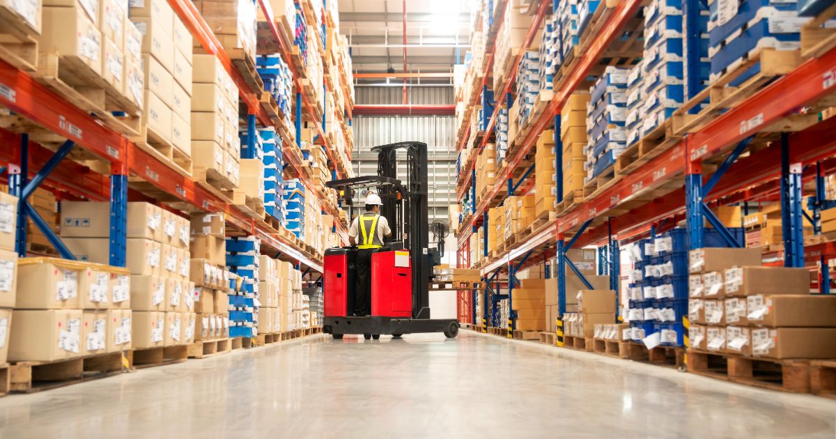 Forklift with employee navigating warehouse aisle.