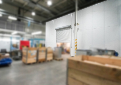 Inside a warehouse, boxes are arranged around a white modular office space with a grey rolling door.