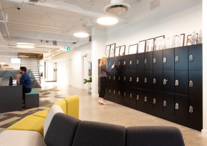 A large office space with black day use lockers and a couch, showing a woman opening a locker.