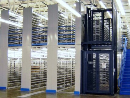 A modern warehouse features towering E-Z-Rect Type 1 shelving units with a dark blue picking tower and staircase for access.