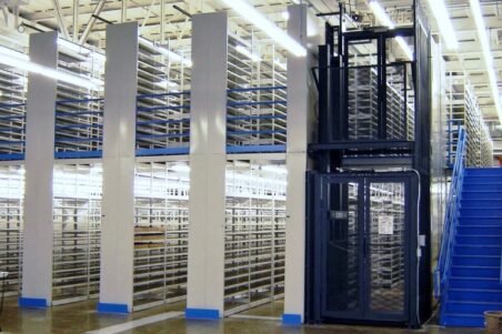 A modern warehouse features towering E-Z-Rect Type 1 shelving units with a dark blue picking tower and staircase for access.