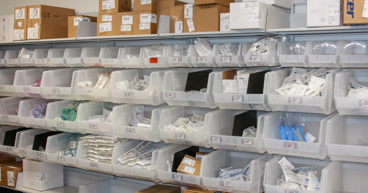 Hi-Cube-Storage-Frame-WRX A storage room wall is fitted with a FrameWRX® shelving system, featuring multiple rows of clear plastic bins filled with various medical supplies