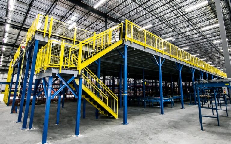 A spacious warehouse with vibrant yellow and blue stairs, featuring a mezzanine storage system.