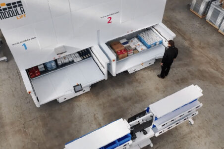 Worker operating two Modula Lift vertical storage units in a clean warehouse.