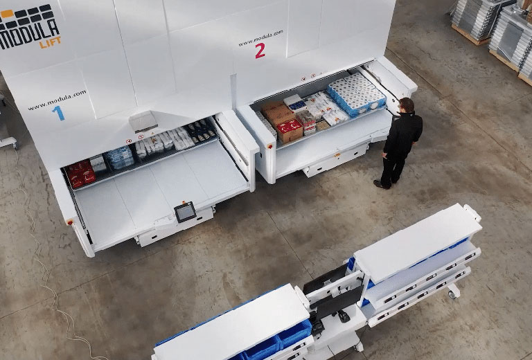 Worker operating two Modula Lift vertical storage units in a clean warehouse.
