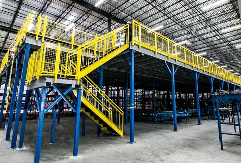 A spacious warehouse with vibrant yellow and blue stairs, featuring a mezzanine storage system.