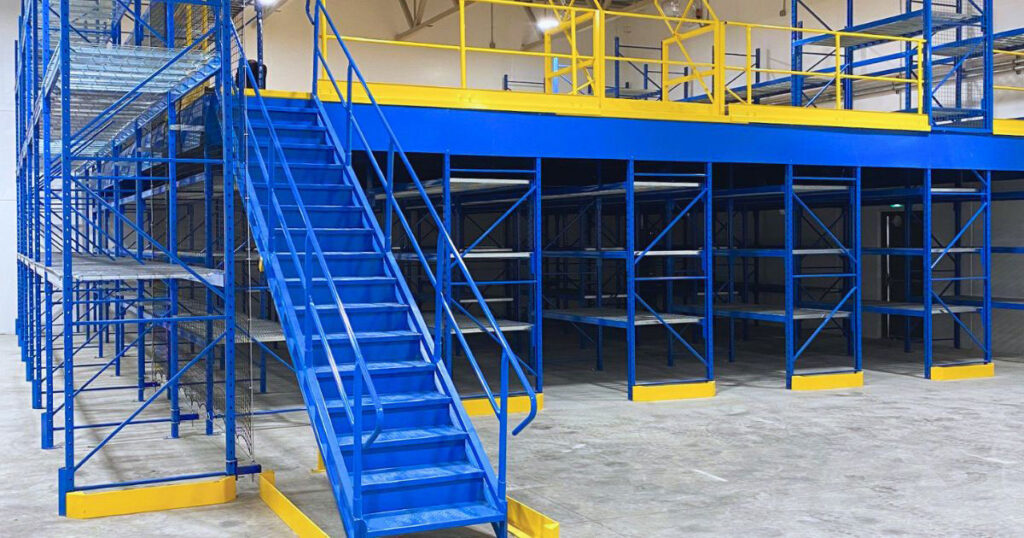 Integrated structural mezzanine work platform featuring blue access staircases and yellow safety guardrails, flanked by multi-tier pallet racking on the side.