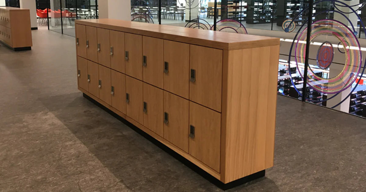 Custom wood-finish day-use locker island with combination locks providing secure personal storage in an academic facility.